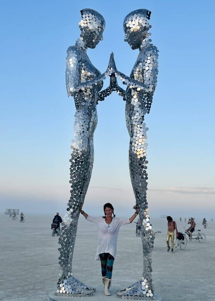 Dalia with a silver sculpture of two metallic tall humanoids appearing out of the air and coming together.