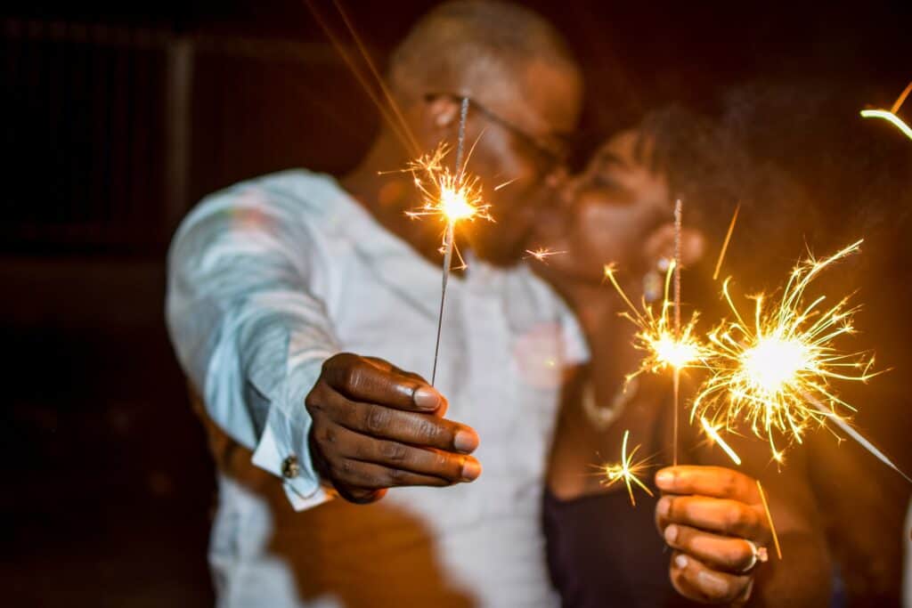 Two people kissing and holding up lit sparklers in celebration.