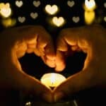 Hands forming a heart over a small candle symbolizing love.