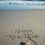 Happy New Years written in the sand of a beach.
